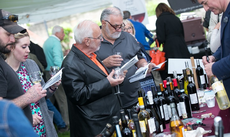 guests reviewing Wine Festival program by table of wine