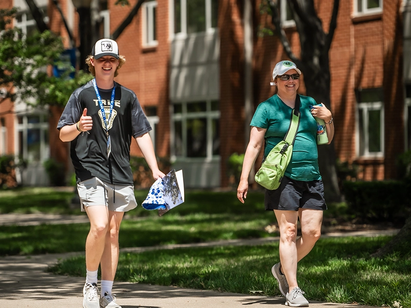 Two St. Ambrose University students walk the St. Ambrose University campus while smiling at the camera