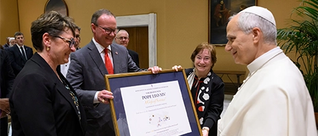 Amy Novak, EdD, president and CEO of St. Ambrose University and Mount Mercy University, presents a framed gift to Pope Leo XIV, alongside other members of the ACCU.