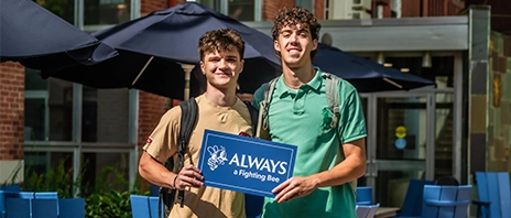 Two students hold a blue sign that reads