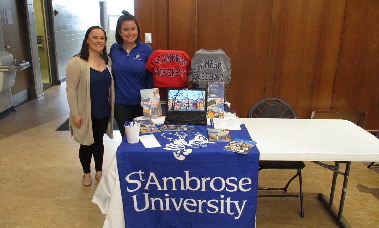 Two female alumni stand by SAU table at college fair