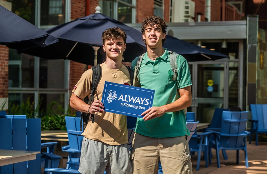 Two students hold a blue sign that reads
