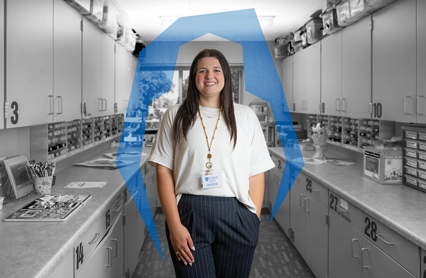 Lauren Posten, '24, '26 MSLP, stands in a lab at St. Ambrose University and smiles into the camera. A blue